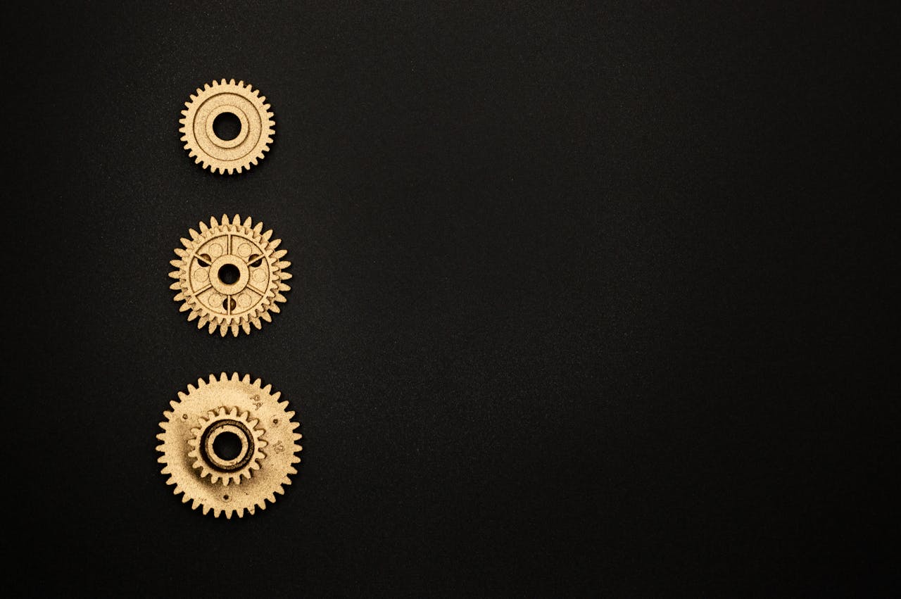 Close-up of three golden gears aligned vertically on a black surface.